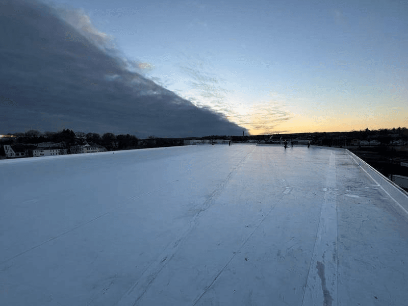 Expansive flat commercial membrane roof with reflective surface under dramatic sky—ideal for TPO, PVC, and other energy-efficient roofing materials